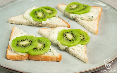 Оформите тост. Хлебные треугольники щедро намажьте сыром с зеленью. Сверху выложите киви.