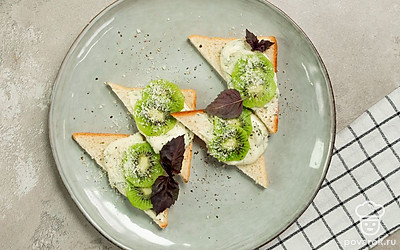 На плоскую сервировочную тарелку выложите тосты с киви, присыпьте их тертым сыром и украсьте листьями базилика.