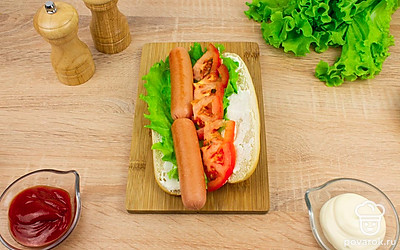 Выложите на булочку лист салата и две сосиски.