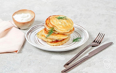 Переложите готовые оладьи в плоскую тарелку, украсьте свежей зеленью и подайте со сметаной. 