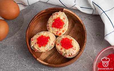 Украсьте фаршированные яйца сверху красной икрой перед подачей на стол.
