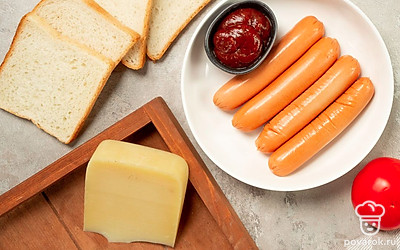 Подготовьте необходимые продукты, удобно расположите их на рабочем столе. Помидоры и зелень для подачи вымойте, обсушите на бумажных полотенцах. Снимите с сосисок упаковку. Зелень и листья салата для подачи вымойте, обсушите на бумажных полотенцах. Подготовьте противень. Включите духовку на 180 градусов.