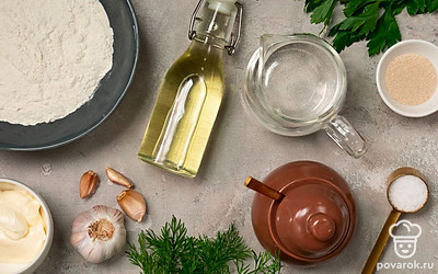 Муку просейте через мелкое сито. Воду слегка подогрейте до температуры выше комнатной. Чеснок очистите и выдавите в прессе. Петрушку и укроп помойте, просушите и мелко нарежьте, оставив листочки с одной веточки петрушки для украшения. Застелите противень пергаментом.