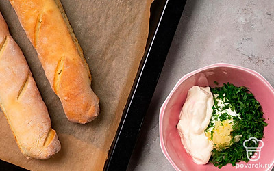 Сделайте соус и добавьте его в багет. В миске соедините майонез, чеснок и нарезанную зелень петрушки и укропа, тщательно перемешайте. Достаньте багет из духовки, сделайте на нем поперечные надрезы в ранее помеченных местах и с помощью силиконовой кисточки распределите по ним соус. Пеките багет еще 10 минут, затем достаньте из духовки и слегка остудите перед подачей.