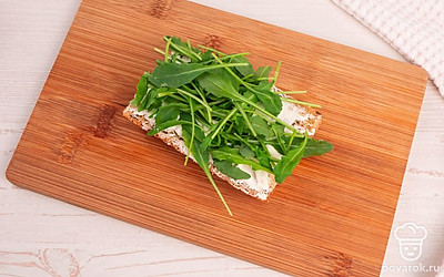 Разрежьте багет пополам. Нанесите на одну половину багета творожный сыр, выложите слой рукколы.