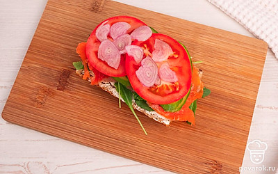 Выложите на рукколу нарезанную семгу, огурцы, помидоры и красный лук.