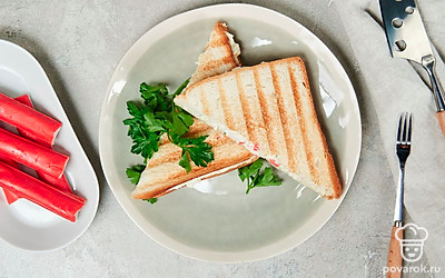 Тост с крабовыми палочками разрежьте по диагонали. Положите ломтики друг на друга, выложите на доску для подачи, украсьте веточкой петрушки.