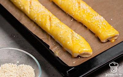 Приготовьте багеты. Тесто выложите на стол, присыпанный мукой, и разделите на 4 части. Из каждой части сформируйте длинный багет. Выложите багеты на противень и острым ножом сделайте косые надрезы. Смажьте багеты взбитым яичным желтком и посыпьте семенами кунжута. Оставьте багеты на расстойку на 40 минут.