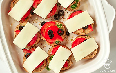 Выложите на багет начинку и запеките его. На кусочки хлеба выложите в следующем порядке: кинзу, помидоры, маслины, сулугуни. Отправьте форму в духовку на 15-20 минут.