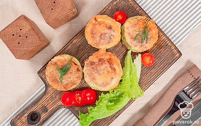 Закуску из фаршированных кабачков лучше подавать к столу теплой, пока не остыл расплавленный в начинке сыр. Для эффектной подачи выложите кабачки на деревянный поднос, предварительно украшенный листьями салата латук и маленькими сочными помидорами черри.