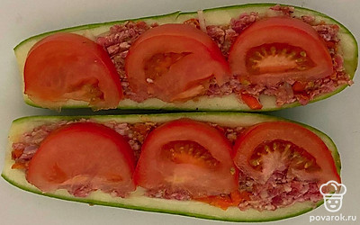 Кабачок разрежьте пополам. Все внутренности кабачка вычислите ложкой. В очищенный кабачок выложите несколько столовых ложек готового фарша. Нарежьте помидору полукольцами и выложите ее поверх фарша.