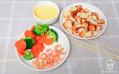 Подавайте сырный соус в специальном приспособлении, чтобы свеча прогревала его. Кусочки багета, овощи и креветки выложите на деревянную доску и подготовьте деревянные шпажки. Процесс употребления фондю - это целый ритуал. Накалывайте кусочки багета, кусочки овощей или креветки на шпажку и макайте в соус.