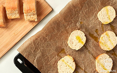 Подготовьте хлеб. Багет нарежьте на кусочки толщиной около 2 см. Выложите на противень, хорошо смазанный маслом. На каждый кусочек налейте приблизительно по 1/2 ч. л. оливкового масла, распределите его по поверхности. На некоторое время оставьте.