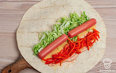 Смажьте часть лаваша, оставив края несмазанными. Положите сверху сыр, капусту, корейскую морковь и сосиску.