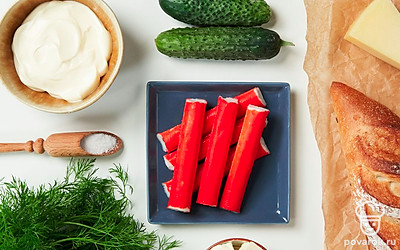 Помойте огурец, обсушите его бумажным полотенцем и, не снимая кожуру, нарежьте мелкими кубиками. Извлеките крабовые палочки из упаковки и мелко нарежьте. Плавленый сыр поместите в морозилку на 10-20 минут. После заморозки натрите его на крупной терке. Укроп ополосните, обсушите и мелко порубите.