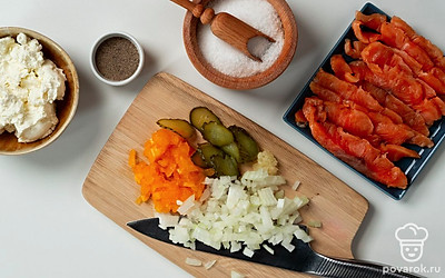 Нарежьте ингредиенты для начинки. Семгу нарежьте маленькими кусочками. Соленый огурец нашинкуйте тонкими ломтиками, а репчатый лук — маленькими кубиками. Чеснок пропустите через пресс, помидор очистите от шкурки, удалите семена, а мякоть мелко порежьте. В одной миске смешайте творожный сыр, нарезанные семгу, лук и помидор, добавьте чеснок, соль и черный молотый перец.