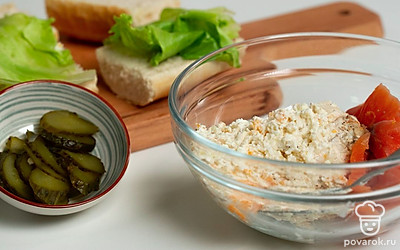 Приготовьте закуску. Багет разрежьте поперек на три части и каждую часть разрежьте вдоль пополам. У нижних половинок багета выньте немного мякиша, оставшийся слегка прижмите. На каждую половинку выложите по одному листу салата, а следом добавьте начинку и кружочки соленых огурцов. Накройте вторыми половинками багета и немного прижмите.