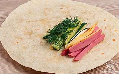 Ближе к середине (как показано на фото) смажьте лаваш майонезом. Сверху положите огурцы, сосиски, сыр и укроп.