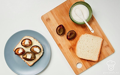 Сформируйте тост. Каждый кусочек хлеба с одной стороны намажьте маслом. Разложите половинки слив сердцевиной вверх. В каждую ямку от косточки положите кусочек сливочного масла и 1/4 ч. л. сахара.