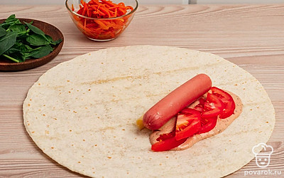 Возьмите лаваш и смажьте приготовленным соусом ближе к середине, отступив от краев 4-5 см. ( используйте для ориентира фото). Сверху на смазанный участок положите помидоры. Рядом сыр и на сыр сосиску.