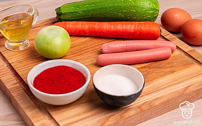 Подготовьте все ингредиенты и выложите их на стол. Помойте кабачок, снимите оболочку с сосисок. Очистите репчатый лук.