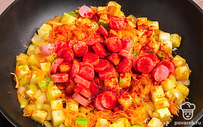 Добавьте в сковороду нарезанные сосиски и паприку. Хорошо перемешайте.