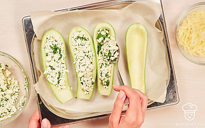 Нафаршируйте и запеките кабачки. Заранее включите духовку на разогрев до 180 градусов. Противень застелите пекарской бумагой или пищевой фольгой. Лодочки из кабачков нафаршируйте творожной начинкой и выложите на противень. Натрите сыр на мелкой терке и посыпьте им начинку сверху. Запекайте кабачки в духовке примерно 40 минут.