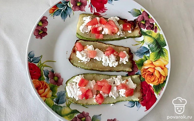 Сыр разотрите вилкой и намажьте им ломтики кабачка. Помидоры нарежьте мелкими кубиками и выложите поверх фетаксы. Сверните кабачки с начинкой в рулетики.