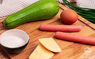 Подготовьте все ингредиенты и выложите их на стол. Помойте кабачок, снимите оболочку с сосисок. Отрежьте необходимо количество сыра. Поставьте духовку на разогрев до 180 С.