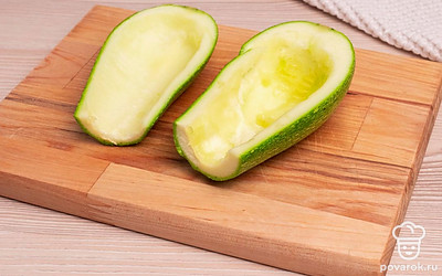 На разделочной доске отрежьте верхнюю часть кабачка. Разрежьте его вдоль на две части и вырежьте середину. Не выбрасывайте ее, она понадобится дальше в приготовлении блюда. Измельчите репчатый лук. Нарежьте сосиски кружочками. Натрите сыр на крупной терке.