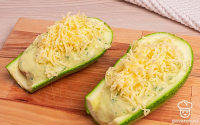 Залейте сосиски в кабачках приготовленной ранее массой и посыпьте тертый сыр.