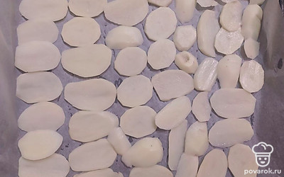 Картофель нарежьте тонкими кружочками. Смажьте противень, застеленный пергаментом растительным маслом, выложите ½ часть картофеля и посолите.