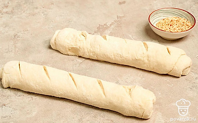 Приготовьте багеты. На рабочую поверхность насыпьте немного муки, выложите тесто, обомните и разделите его на две равные части. Из каждого кусочка сформируйте багет. Поместите будущий хлеб на противень, застеленный пергаментной бумагой. С помощью ножа сделайте косые надрезы. Смажьте тесто молоком и посыпьте кунжутом. Оставьте багеты еще на полчаса. Затем противень с багетами поставьте в разогретую духовку на 20 минут.