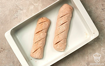 Сформируйте багеты. Готовое тесто разделите на 2 одинаковые части. Затем слепите из них 2 похожих друг на друга багета. С помощью ножа сделайте косые надрезы по всей поверхности теста и поместите будущие багеты в форму для выпечки. Поставьте багеты выпекаться. Включите духовку разогреваться до 200 градусов. На дно духовки поставьте емкость с водой. Форму поместите на средний уровень и оставьте тесто выпекаться на 30 минут.