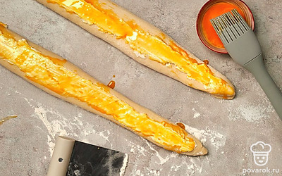 Поставьте багет выпекаться. За 20 минут до начала выпечки включите духовку на 250 градусов, чтобы она разогрелась. На дно духовки поставьте миску с водой. Смажьте тесто яичным желтком и распределите по нему оставшиеся 50 г сыра. Поставьте заготовки выпекаться на 10 минут. Затем уберите миску, снизьте температуру до 200 градусов и оставьте багеты в духовке еще на 15 минут.