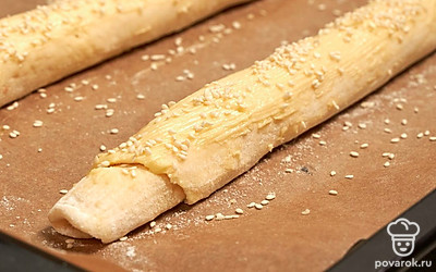 Сформируйте и испеките багеты. Достаньте тесто из холодильника, раскатайте каждую часть в прямоугольник и скрутите в рулет. Выложите багеты на противень, смажьте их сливочным маслом и посыпьте кунжутом. Сделайте по три надреза на каждом багете под углом 30 градусов. Поставьте тесто в теплую духовку на 30 минут, чтобы багеты увеличились в объеме в два раза. Выпекайте багеты в разогретой до 180 градусов духовке в течение 30 минут.