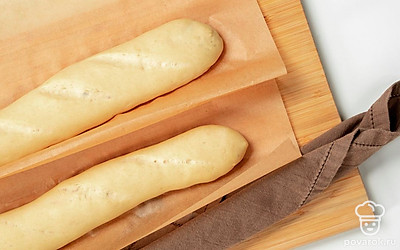 Подготовьте багет к выпечке. На противень выложите лист пергаментной бумаги. Сверху расположите будущий хлеб. С помощью ножа сделайте на поверхности теста косые надрезы. Затем сверните два полотенца в небольшие жгуты и подложите их под пергамент, подпирая багет с двух сторон. Оставьте тесто при комнатной температуре на 20-30 минут. В это же время включите духовку разогреваться до 200 градусов.