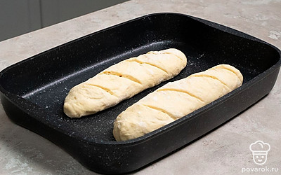 Испеките багеты. Пока тесто “отдыхает”, включите духовку на 250 градусов. Затем сделайте на изделиях надрезы наискосок, выложите на противень. На нижнюю полку духового шкафа поставьте емкость с водой, в средний отдел — противень с багетами. Выпекайте в течение 20 минут, затем нагрев убавьте до 220 градусов и пеките багеты еще 15 минут.