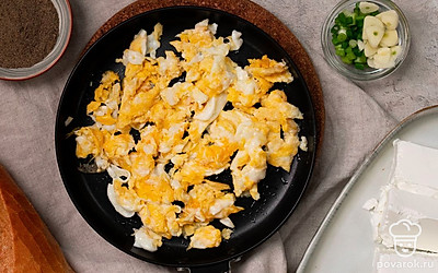 Приготовьте яйца-скрэмбл. В толстостенный сотейник разбейте яйца, добавьте сливочное масло, измельченный лук и чеснок. Включите слабый огонь. Постоянно помешивая, дайте яйцам немного схватиться. Ориентировочное время готовки — 6-7 минут. Затем выключите огонь, добавьте в сотейник брынзу, приправьте перцем, перемешайте.