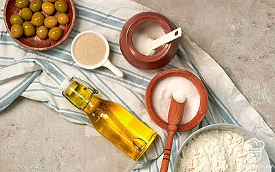 Муку просейте. Оливки нарежьте колечками. Воду вскипятите и остудите до теплого состояния. Духовку разогрейте до 200 градусов.