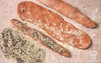 Сформируйте багеты. Разделите тесто на 3 части. Сформируйте багеты руками, сначала слегка растягивая тесто, а затем раскатывая его ладонями по столешнице, присыпанной ржаной мукой. На столе смешайте мак, кунжут и кориандр, мокрыми руками оботрите поверхность багета и обваляйте его в обсыпке. Слегка придавите тесто.