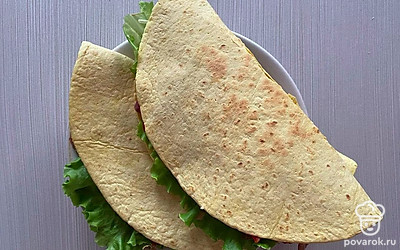 На уже обжаренную лепешку, на одну половину выложите соус, на другую положите лист салата, на сторону с соусом выкладывайте фасоль, обжаренные овощи, сыр и зелень. Накройте овощи другой половиной лепешки, можно подавать к столу.