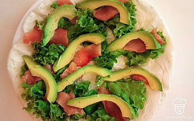 На тортилью, либо лаваш намажьте слой сливочного сыра, сверху выложите слой из листьев салата. Тонко нарежьте рыбу, и также выложите ее на лаваш.