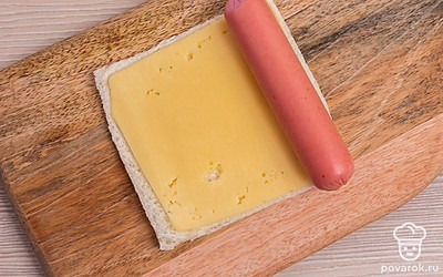 Сверху положите целую сосиску. И сверните хлеб плотным рулетиком.