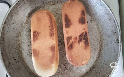 Соленые огурцы нарежьте длинными ломтиками.На сухой сковороде поджарьте булочки со всех сторон. Разрежьте поджаристые булочки с одной стороны, но не до конца.Смажьте булочки внутри горчицей и кетчупом. Во внутрь булочек вложите соленые огурцы. На огурцы выложите по сосиски. На сосиски выложите жареный лук.