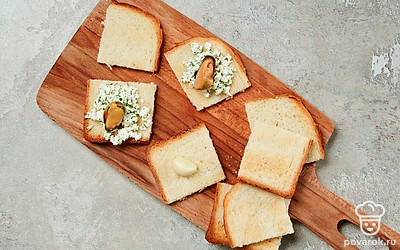 Приготовьте тосты. Подсушенный хлеб разрежьте на 4 равные части, натрите каждый кусочек чесноком с двух сторон. Выложите на хлебный кусочек начинку, сверху распределите мидии.