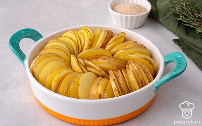 Нарежьте картофель с кожурой очень тонкими круглыми ломтиками, толщиной не более 1 мм. Разложите его в форме для запекания, ставя ломтики вертикально по кругу вдоль бортиков формы и в оставшемся пространстве в центре формы.