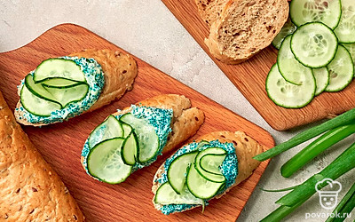 Соберите закуску. Багет и огурец нарежьте на кружочки, помидор — половинками кружочков. На кусочек багета распределите намазку, а сверху выложите ломтик огурца. То же самое повторите на другом кусочке багета, заменив огурец на помидор. Продолжайте комбинировать бутерброды с овощами до тех пор, пока не закончатся продукты.