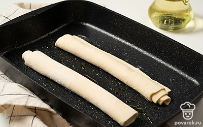 Сформируйте багеты. Тесто разделите на две части. Каждую часть раскатайте в тонкий пласт, сверните рулетом и выложите на противень, смазанный растительным маслом. Оставьте багеты на 30 минут расстаиваться.