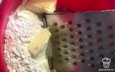 Насыпьте муку и 1 столовую ложку сахара в чашку. Перемешайте. Масло протрите через терку вместе с мукой, чтобы получилось рассыпчатое тесто.